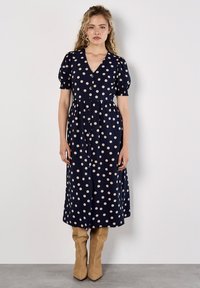 Marineblaues Kleid mit V-Ausschnitt, kurzen Puffärmelchen und großen cremefarbenen Punkten. Es hat eine knopf-bis-Front und einen knielangen Rock.