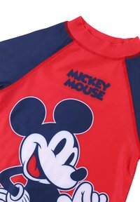 Rash guard rosso e blu navy con una grande grafica di Topolino, texture liscia, colletto alto e cuciture a contrasto.