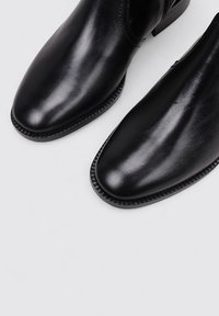 Botas de cuero negras con una punta afilada y superficie lisa. Las costuras de acentuación a lo largo de la suela añaden detalle y textura.