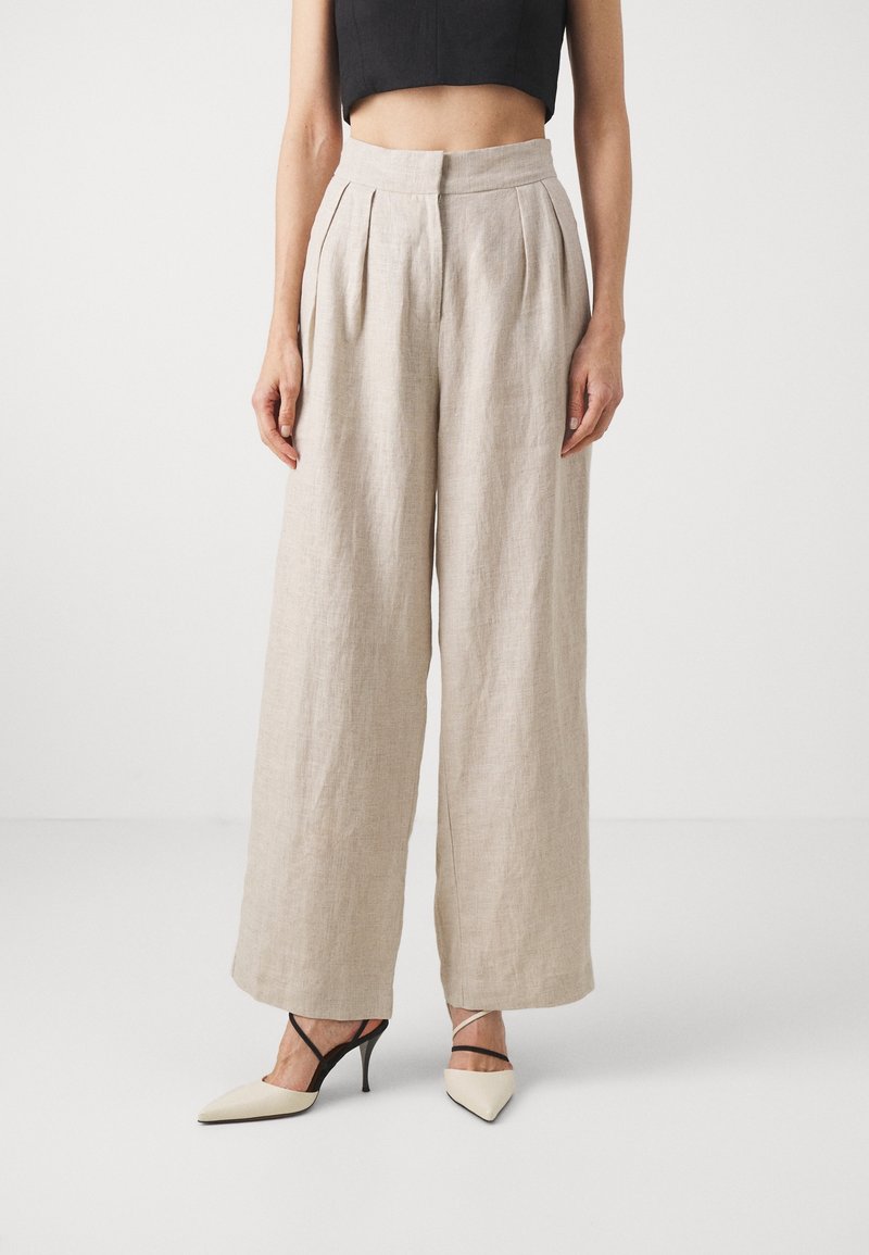 Beige linne vida byxor med veck och hög midja. Kombineras med spetsiga klackar med svarta korsade remmar.