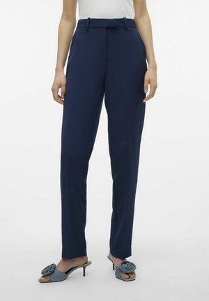 Pantalones ajustados azul marino con una textura suave, lazos para cinturón y un corte recto, combinados con tacones abiertos de punta azul claro con un acento de flor.