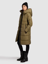 Oliiviroheline tepitud mantel kõrge krae ja kapuutsiga, millel on tõmblukuga küljetaskud, kombineeritud mustade retuuside ja põlvekõrguste saapadega.