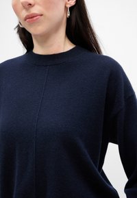 Tengerészkék, gyapjú keverék pulóver, amely kör alakú nyakkivágással és eső vállakkal rendelkezik, puha tapintású és minimális varrási részletezéssel.