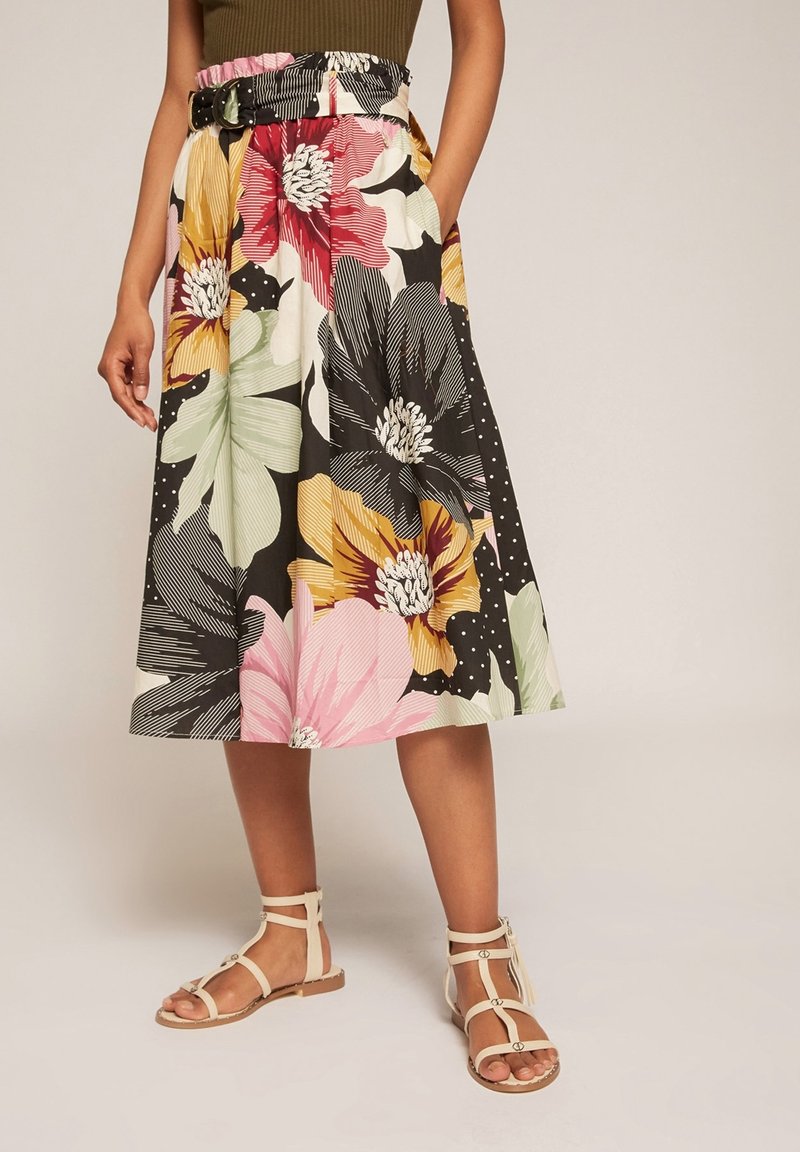 Floral skirt with a black base, featuring large pink, yellow, and green flowers, and a wide belt loop. Paired with beige sandals.