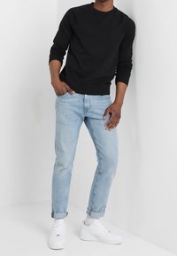 Černá mikina s kulatým výstřihem, spárovaná se světle modrými tapered džíny. Obuv tvoří bílé tenisky. Jednoduchý design s ležérním střihem.