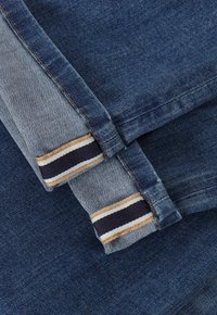 Tela de mezclilla en tonos azules variados. El puño presenta un patrón a rayas en colores beige, navy y crema. Textura con un acabado suave.
