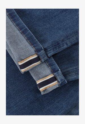 Tela de mezclilla en tonos azules variados. El puño presenta un patrón a rayas en colores beige, navy y crema. Textura con un acabado suave.