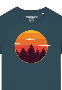 Donker teal T-shirt met een cirkelvormige afbeelding van een zonsondergangsverloop in oranje en paars, omhulde dennenbomen en witte wolken.