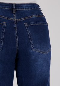 Donkerblauwe denim jeans met een middelhoge taille, twee achterzakken en contrasterend stiksel langs de naden. Soepele textuur.