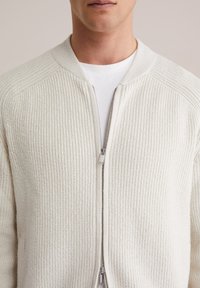 Helebeežika helepruun tikkribaga lukuga kardigan, ümar kaelus ja hõbedane tõmblukk. Omab kahte küljetaskut ja keha järgivat lõiget.