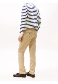 Gestreifter Pullover in Marineblau und Weiß, beiger Hose und dunkle Loafers; sichtbare Nähte und Taschen-Details verfeinern das Design des Outfits.