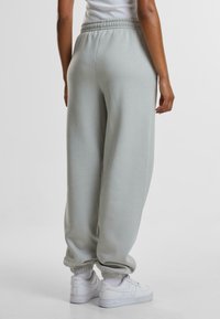 Lys grå joggebukser med en avslappet passform, elastisk midje og ribbede ankler, kombinert med hvite joggesko. Glatt bomullsmateriale.
