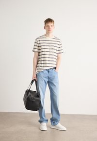 Tricou striped bej și marin, blugi albaștri deschiși, ținând o geantă neagră. Tenisii albi completează ținuta casual.