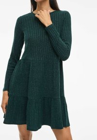 Robe à manches longues côtelée de couleur vert foncé, avec un ourlet évasé et un design en volants superposés. Fabriquée en tissu texturé, elle présente un col rond.