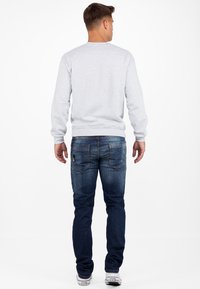 Sweatshirt gris avec des poignets côtelés, associé à un jean en denim bleu foncé avec des poches arrière et un léger délavage, complété par des baskets blanches.