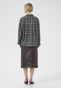 Woman with short blonde hair wearing a black and white checkered shirt, dark brown leather skirt, and black heeled sandals, facing away.