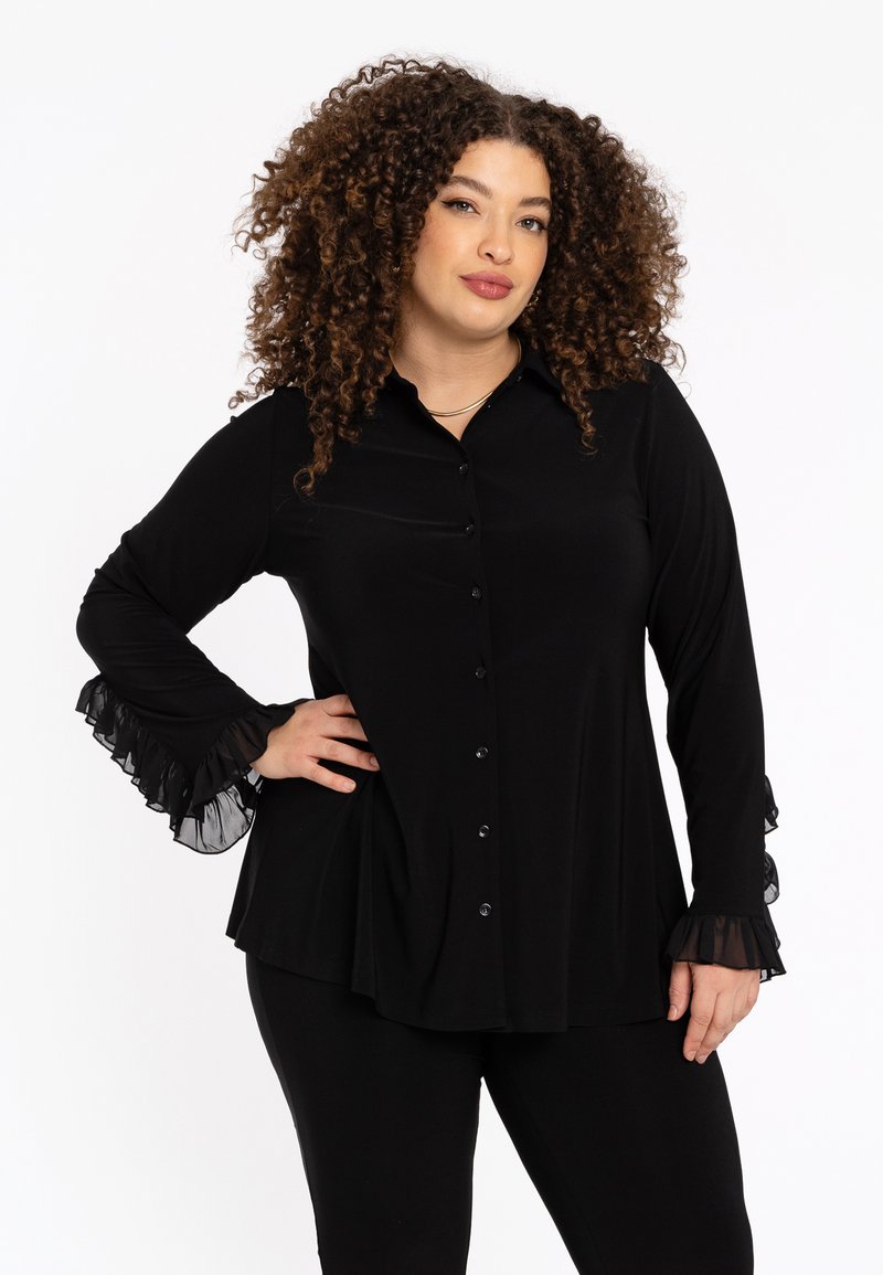 Zwarte blouse met een knoopsluiting aan de voorkant, lange mouwen en rimpelige doorschijnende accenten bij de manchetten. Gemaakt van een gladde stof met een vloeiende ontwerpen.