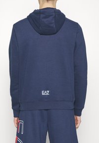 Marinblå hoodie i bomullsblandning med en kenguruficka, ribbade ärmslut och nederkant; har EA7-logotypen på den nedre delen av ryggen.