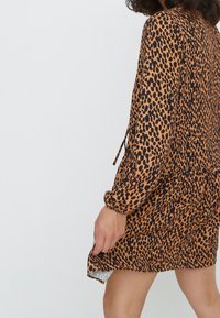 Sukienka w panterkę w kolorze pomarańczowym i czarnym. Długie rękawy o luźnym kroju. Posiada lekko rozszerzaną formę oraz boczne rozcięcia u dołu.