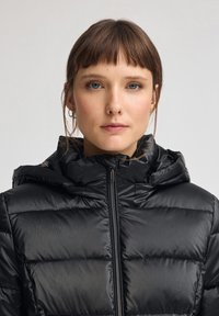 Czarna kurtka puchowa z zamkiem błyskawicznym z przodu, kapturem i pikowaną powierzchnią. Posiada metaliczne elementy i delikatny połysk. Odpowiednia na chłodniejszą pogodę.