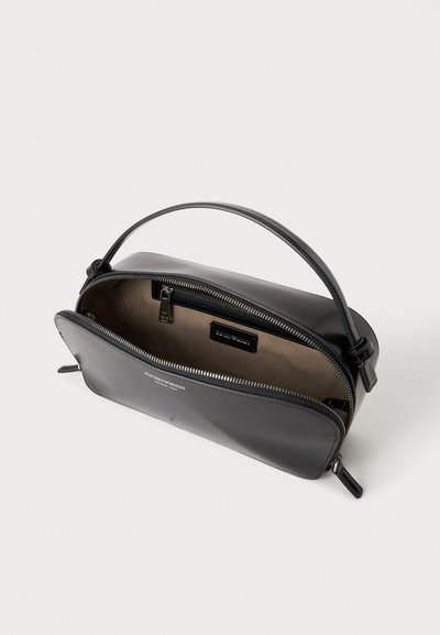 Sac à main en cuir noir avec une seule poignée et une fermeture éclair ouverte montrant un intérieur beige et une poche intérieure zippée.