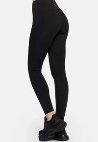 Black leggings with a high waist, smooth texture, and fitted design. Features contrasting stitching and paired with black athletic shoes.