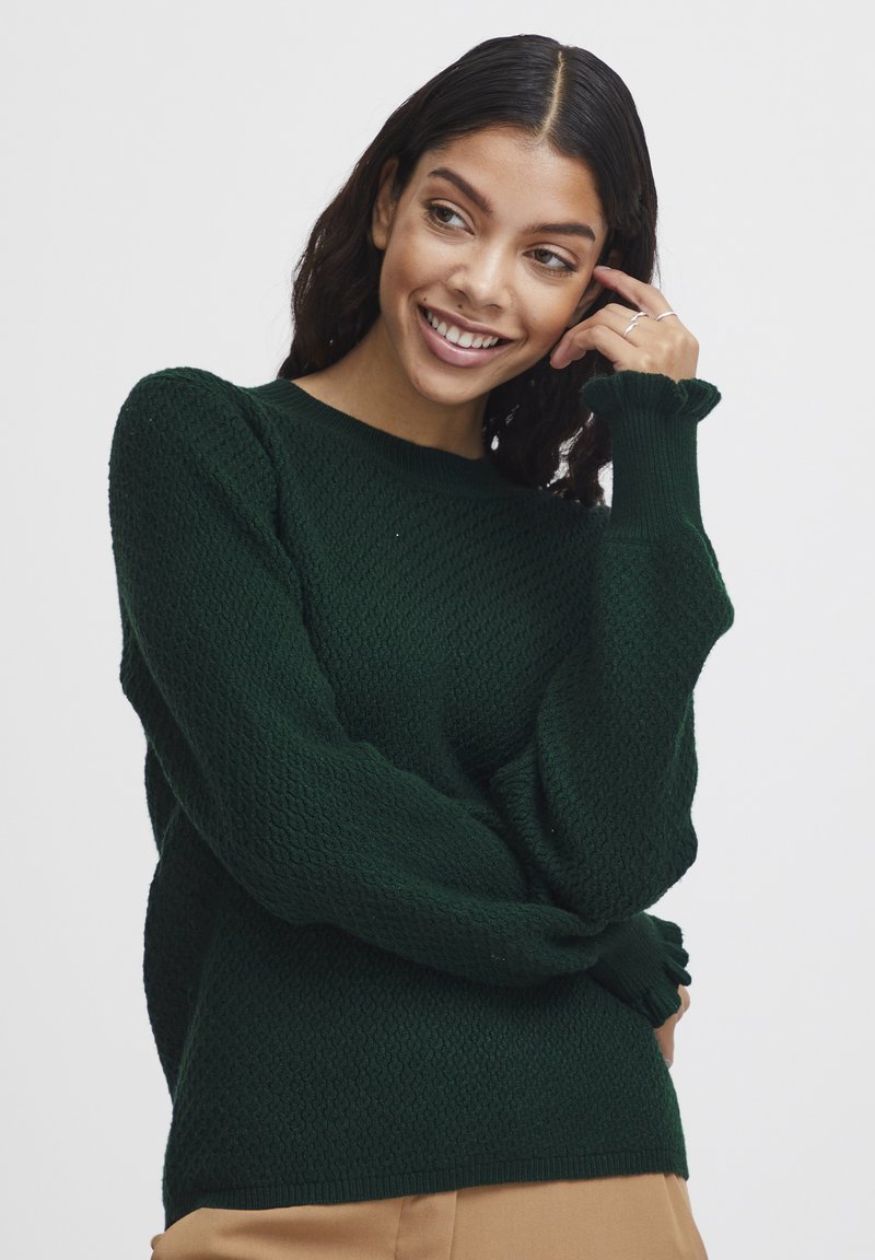 Dunkelgrüner gestrickter Pullover mit einem strukturierten Muster, langen Ärmeln und Rüschensäumen. Der Kragen ist rund, und der Schnitt ist lässig.
