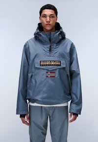 Blue, wind-resistant jacket with a quarter zip, adjustable hood, and "Napapijri" logo. Features a Norwegian flag patch and side pocket.