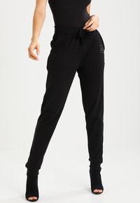 Black jogger pants featuring a drawstring waist, side pockets, and ribbed cuffs, made of soft fabric with a small logo patch.