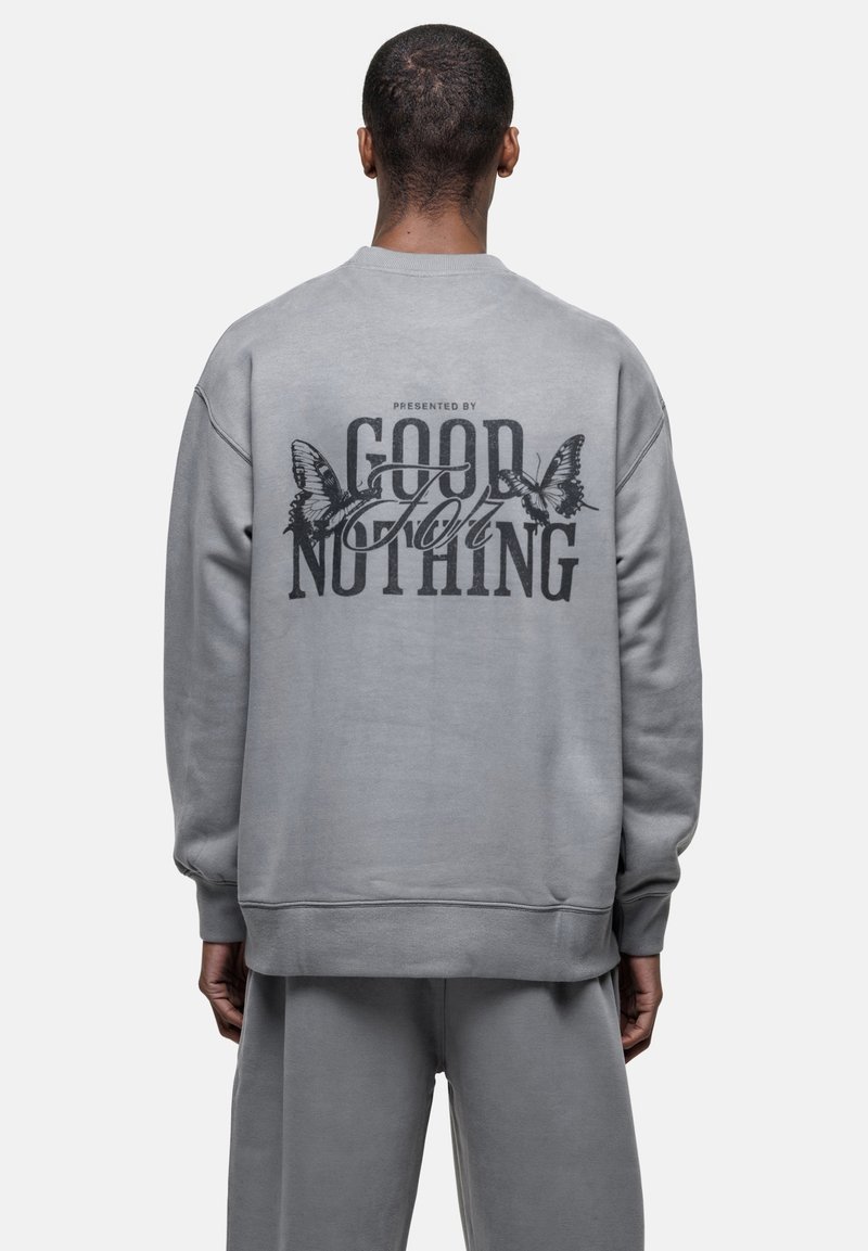 Felpa grigia con maniche lunghe, caratterizzata da una grande grafica nera sul retro con il testo "GOOD FOR NOTHING" e illustrazioni di farfalle.
