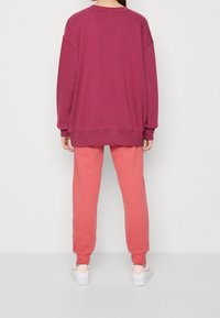 Överdimensionerad bourgogne sweatshirt med sänkt axel, matchad med ljus korallfärgade tapered sweatpants och vita sneakers.