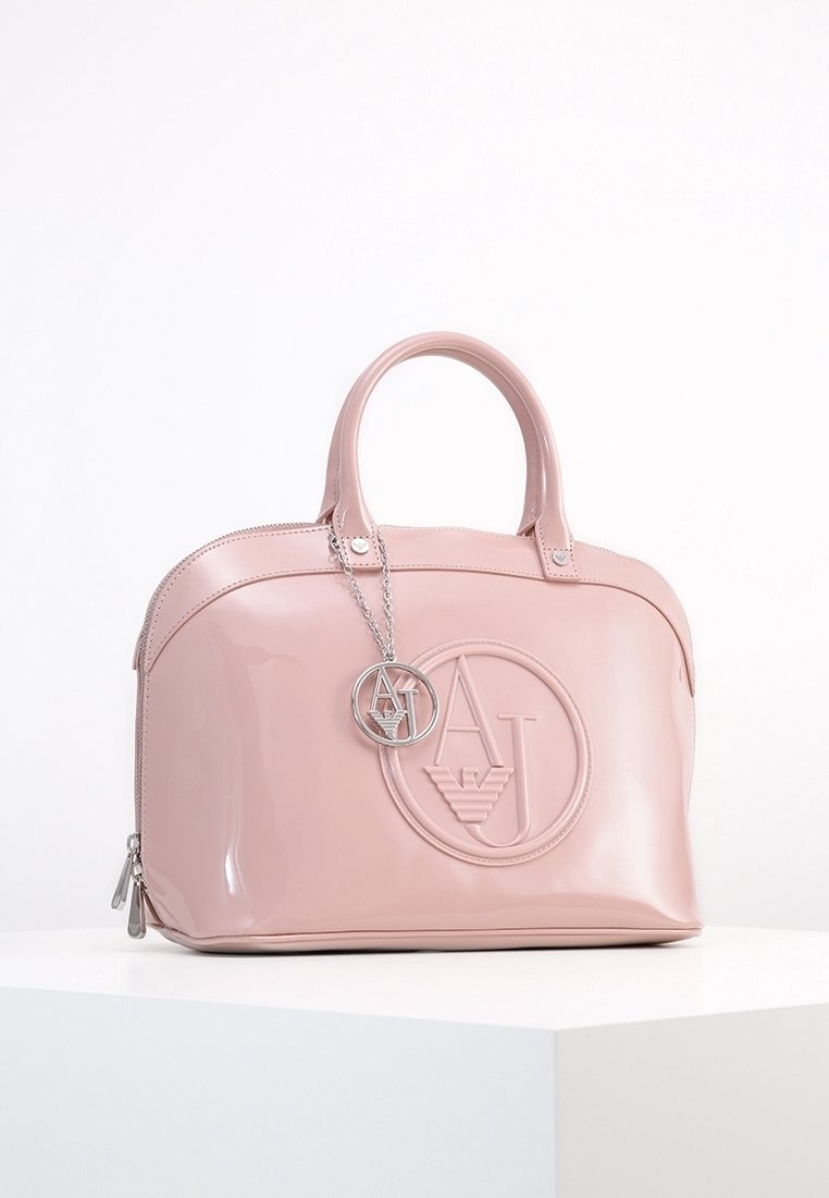 Różowa torebka z lakierowanej skóry w zaokrąglonym kształcie, z wyraźnym wytłoczonym logo oraz srebrnym łańcuchem z zawieszką z logo.