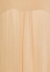 Tissu de robe couleur pêche avec une texture douce et transparente, présentant un corsage incurvé et des plis verticaux pour plus de détails.