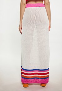 Witte gebreide maxi rok met een roze tailleband en kleurrijke horizontale strepen aan de onderkant, met oranje, blauwe en paarse accenten.