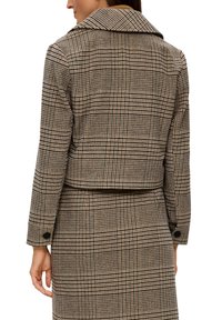 Brązowa krótka kurtka w kratę z dużym kołnierzem, długimi rękawami i guzikami. Posiada fakturowany materiał w kratkowany wzór.