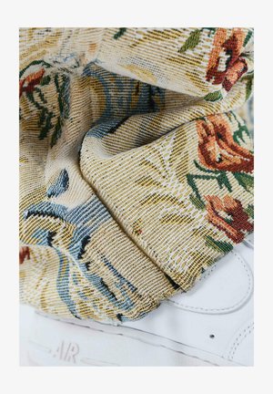 Weiße Sneaker mit strukturiertem, floral gemustertem Stoffbund in Gelb, Blau und Rot. Detaillierte Nähte und weiches, gewebtes Material sind sichtbar.