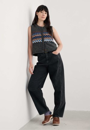 Pull sans manches gris avec un motif en zigzag multicolore, assorti à un jean noir ample et des sabots en bois marron. Texture lisse, design décontracté.