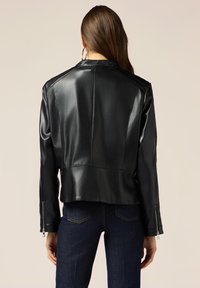 Giacca nera in pelle sintetica con un design crop, cuciture sulle spalle e zip silver sulle maniche. Texture liscia e vestibilità sartoriale.