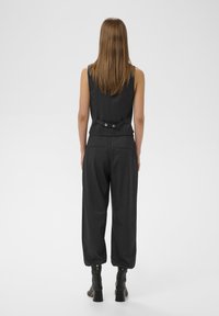 Mono negro entallado con top sin mangas, diseño estructurado, detalles de botones en la parte trasera y pantalones tapered de corte relajado.