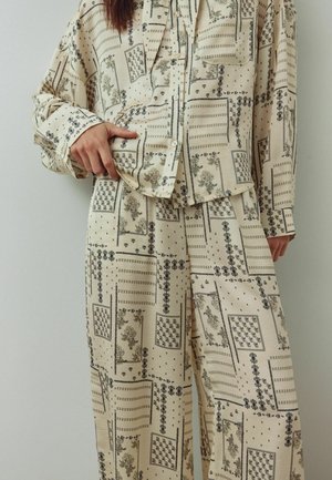 Bēša rakstaina apģērba komplekts ar pogām aiztaisāmu kreklu un platām biksēm. Dizains ietver tumšos toņos ziedu un ģeometriskus rakstus.