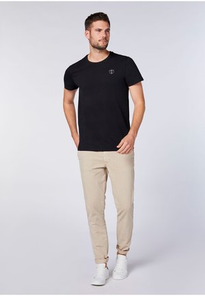 Black short-sleeve t-shirt with a crew neckline and a small logo, paired with beige slim-fit trousers and white sneakers.