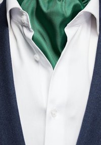 Vit skjorta med detaljer i form av knappar, lager på lager under en grön satin scarf, kombinerad med en blå texturerad jacka, med fokus på tyg- och färgkontrast.