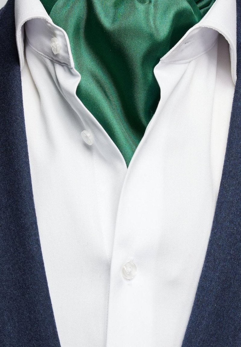 Vit skjorta med detaljer i form av knappar, lager på lager under en grön satin scarf, kombinerad med en blå texturerad jacka, med fokus på tyg- och färgkontrast.