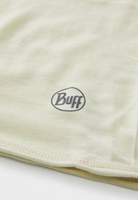 Lysegul Buff-mærke stof med en blød tekstur, der har et trykt logo i mørkeblå. Kanten har en subtil stikdetalje.