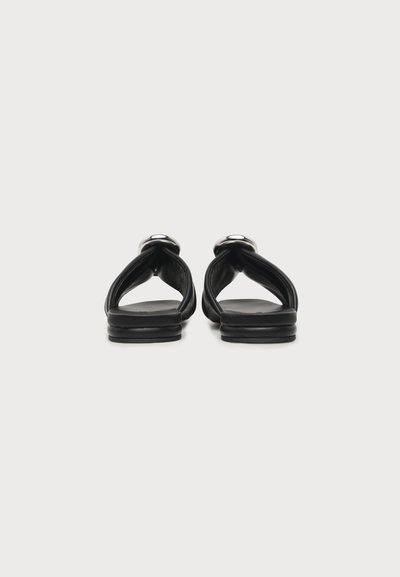 Paire de sandales plates noires avec brides rembourrées et détail de boucle argentée, vues de dos sur fond blanc.