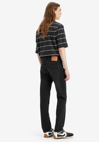 Schwarze Jeans im geraden Schnitt, kombiniert mit einem schwarz-weiß gestreiften T-Shirt. Die Sneakers haben ein auffälliges geometrisches Design.