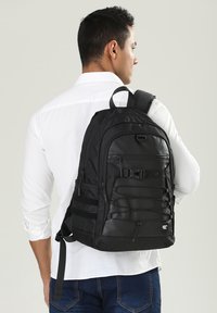 Zaino nero realizzato in materiale resistente, con spallacci regolabili, numerosi scomparti e un design frontale con corda bungee per un ulteriore spazio di stoccaggio.