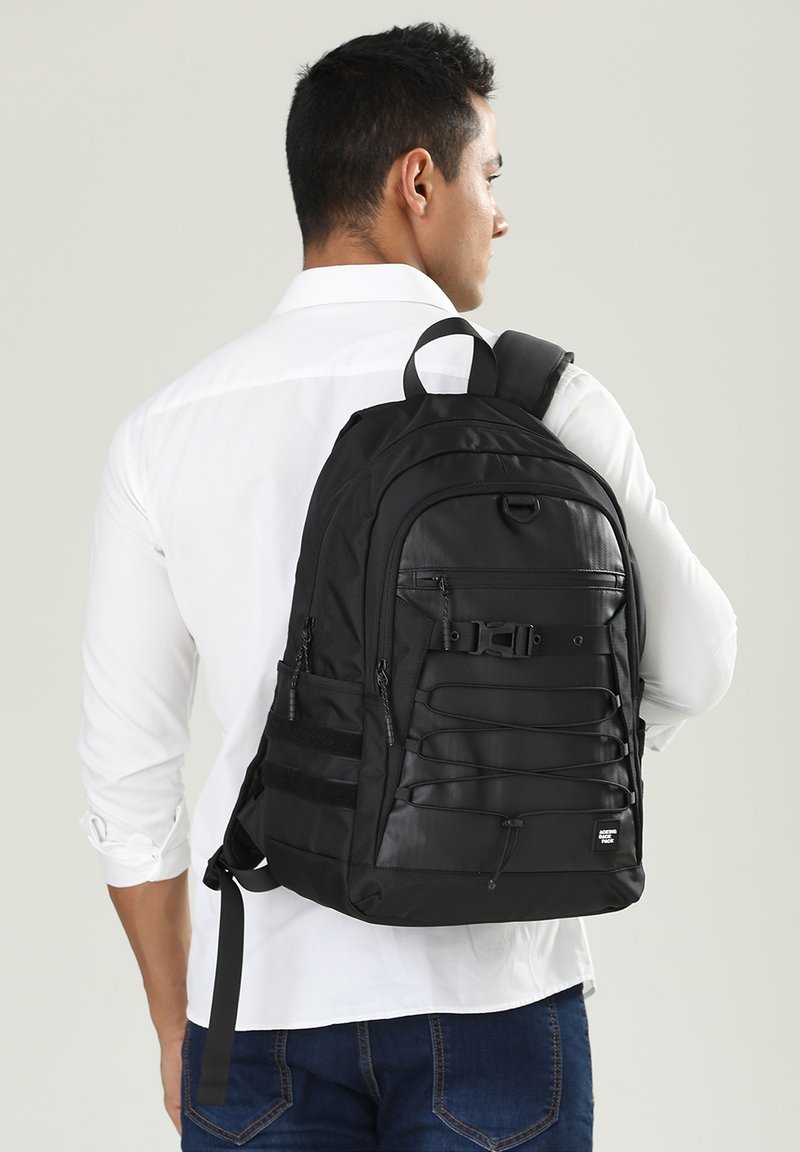 Sac à dos noir en matériau durable, avec des bretelles ajustables, plusieurs compartiments et un design à cordon élastique à l'avant pour un rangement supplémentaire.