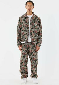 Chaqueta y pantalones de mezclilla con un estampado floral en verde oscuro, con rosas en tonos rosa y beige. Una camiseta blanca y zapatillas completan el conjunto.