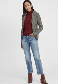 Grå stickad cardigan med ett texturerat mönster, bruna knappar, bärs över en vinröd ribbad polotröja, kombinerad med ljusblå tapered jeans och bruna stövlar.
